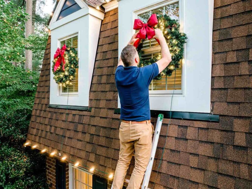 christmas light installer hanging a wreath on a home